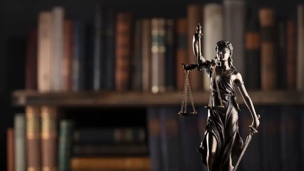 Lady Justice statue with scales and sword in front of blurred bookshelves.